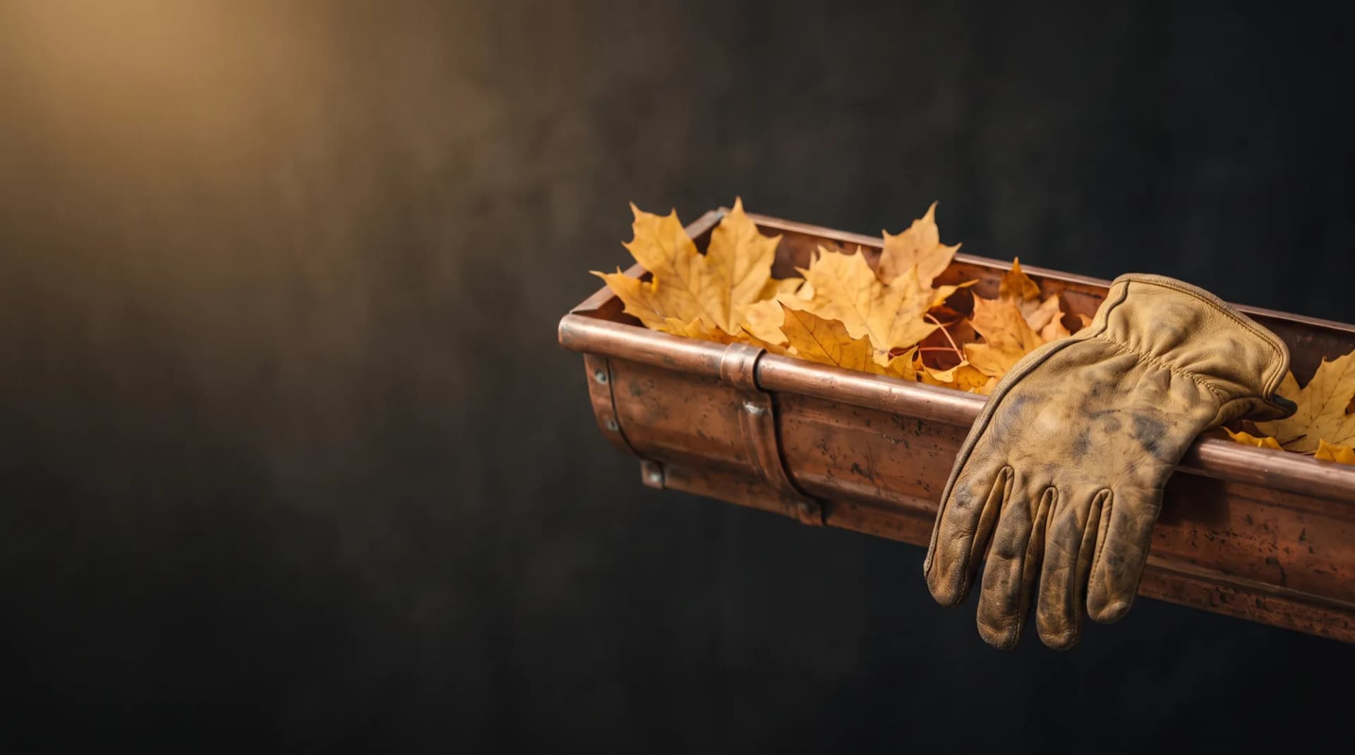 A copper eavestrough filled with golden autumn maple leaves, a worn leather work glove resting on its edge.