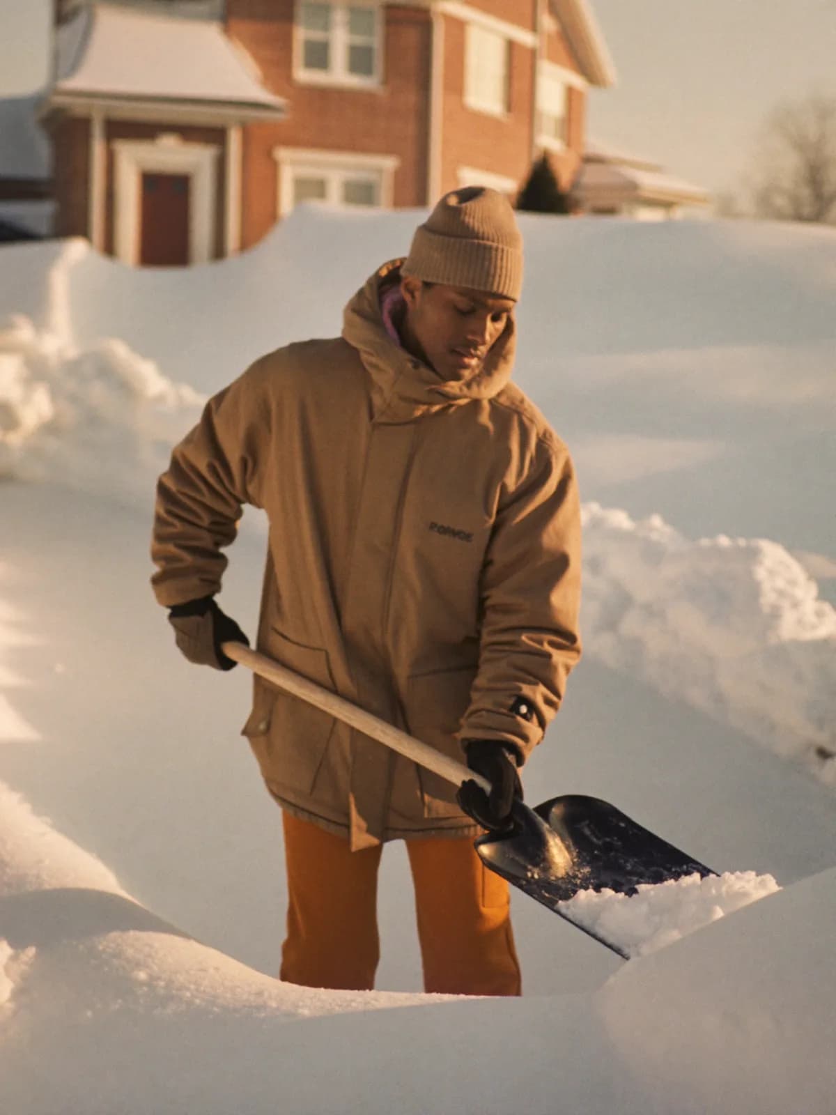 A Tasker in a warm parka shoveling fresh snow from a Toronto driveway at golden-hour sunrise.