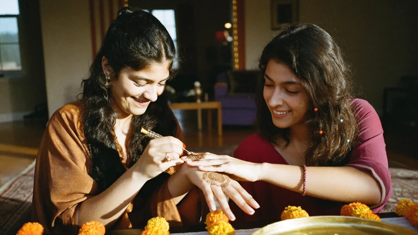 A mehndi artist piping a henna pattern onto an open palm, marigolds on the table.