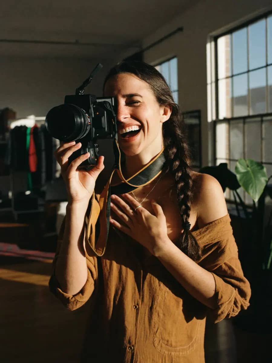 A photographer laughing at the shot she has just taken, camera still raised.